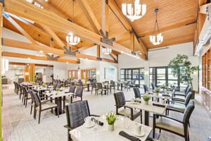 Spacious dining area with wooden vaulted ceiling, numerous tables, and large windows