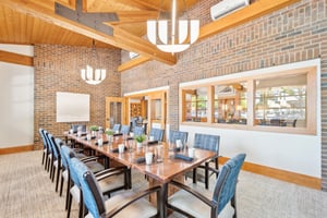 Dining area with long wooden table, blue chairs, and brick walls