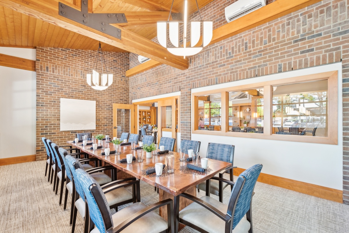 Dining area with long wooden table, blue chairs, and brick walls