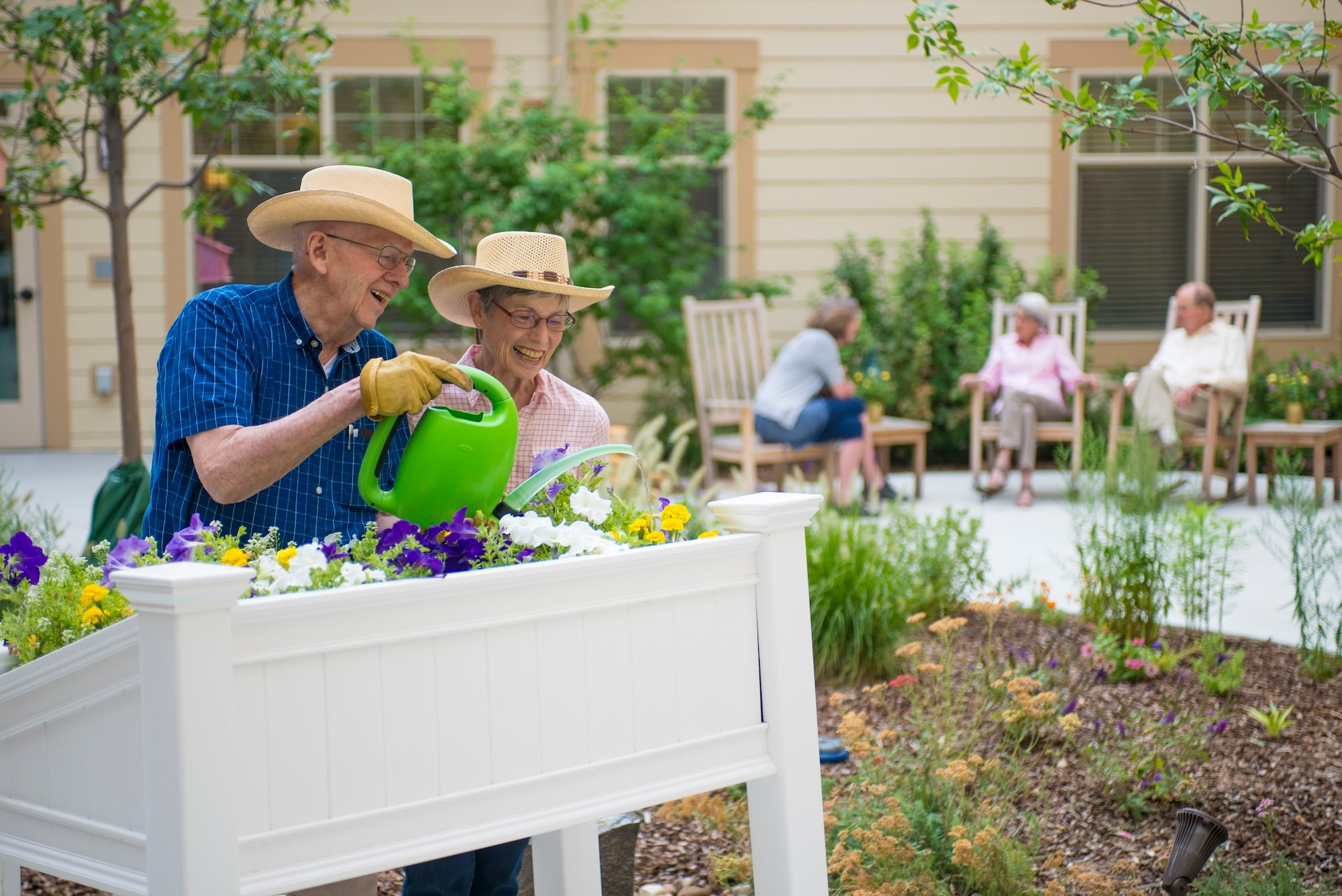 two seniors smiling while they water their flower raised garden bed