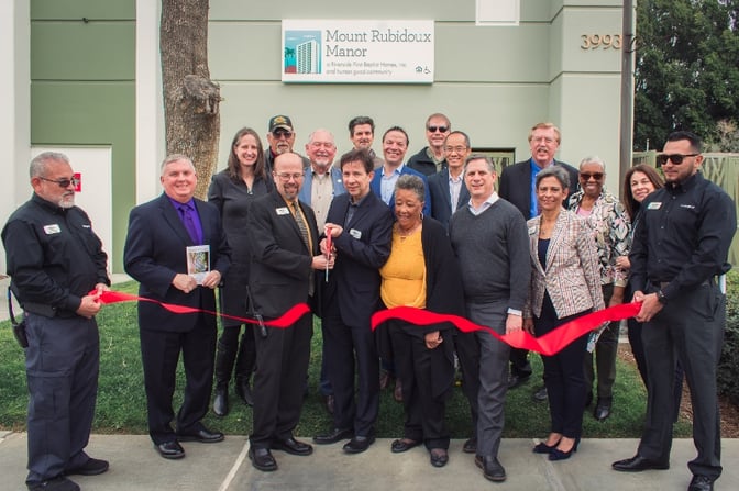 A group of people cutting a ribbon in front of a building with a sign that says Mount Rubidoux Manor.