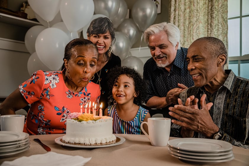 Senior woman blowing out the candles on a birthday cake surrounded by friends and family