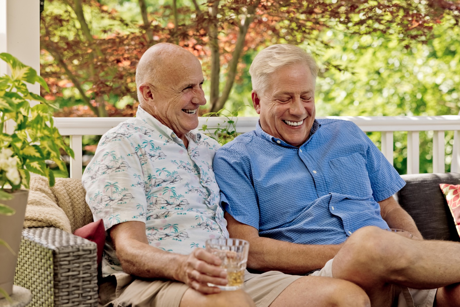 Two senior men holding drinks and sitting outdoors 