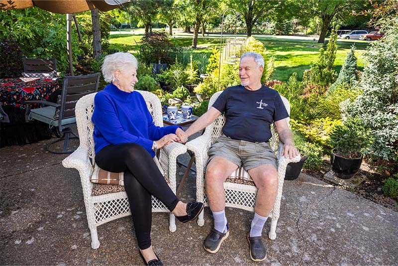 Senior couple holding hands while sitting in wicker chairs on patio