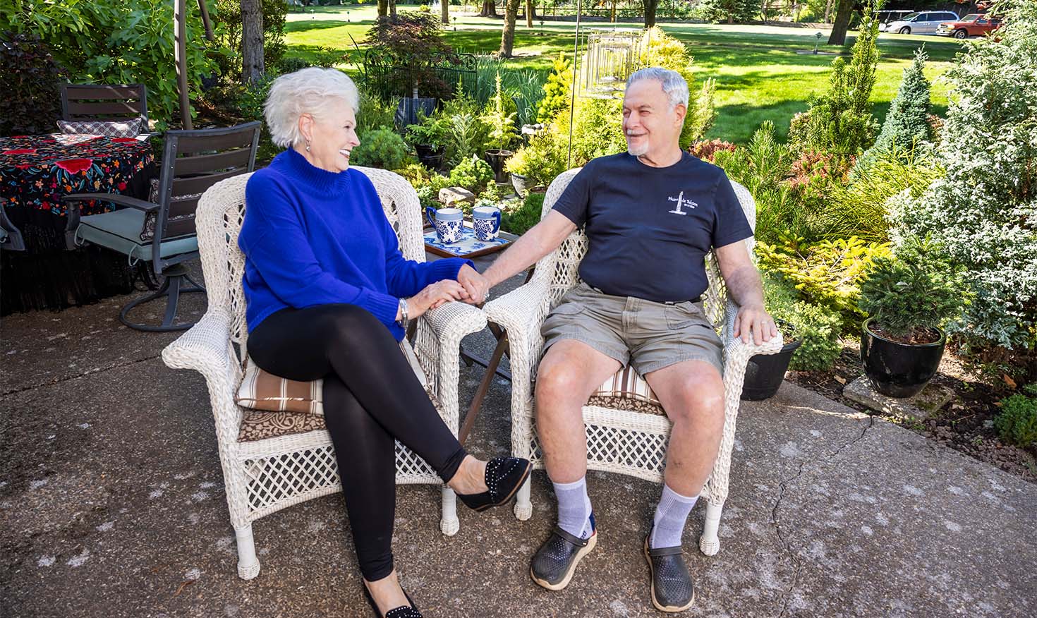 A senior couple holding hands while sitting in wicker patio chairs outside