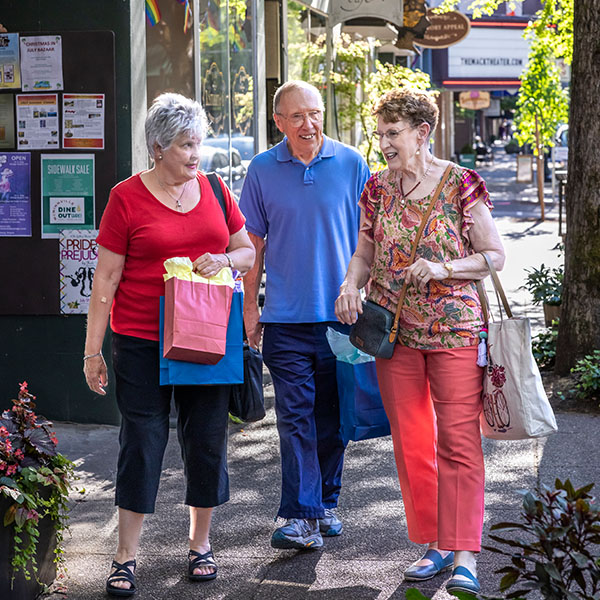 A group of seniors walking on on the sidewalk of a small downtown area holding shopping bags