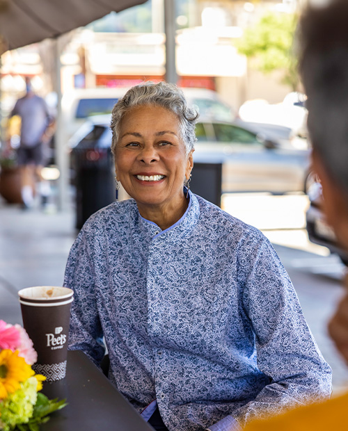 Senior woman sitting at a cafe patio drinking coffee with a friend