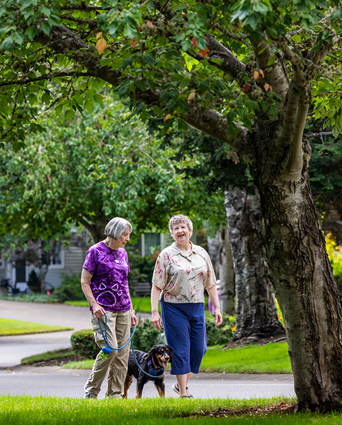Two senior women walking dog together in a nice neighborhood