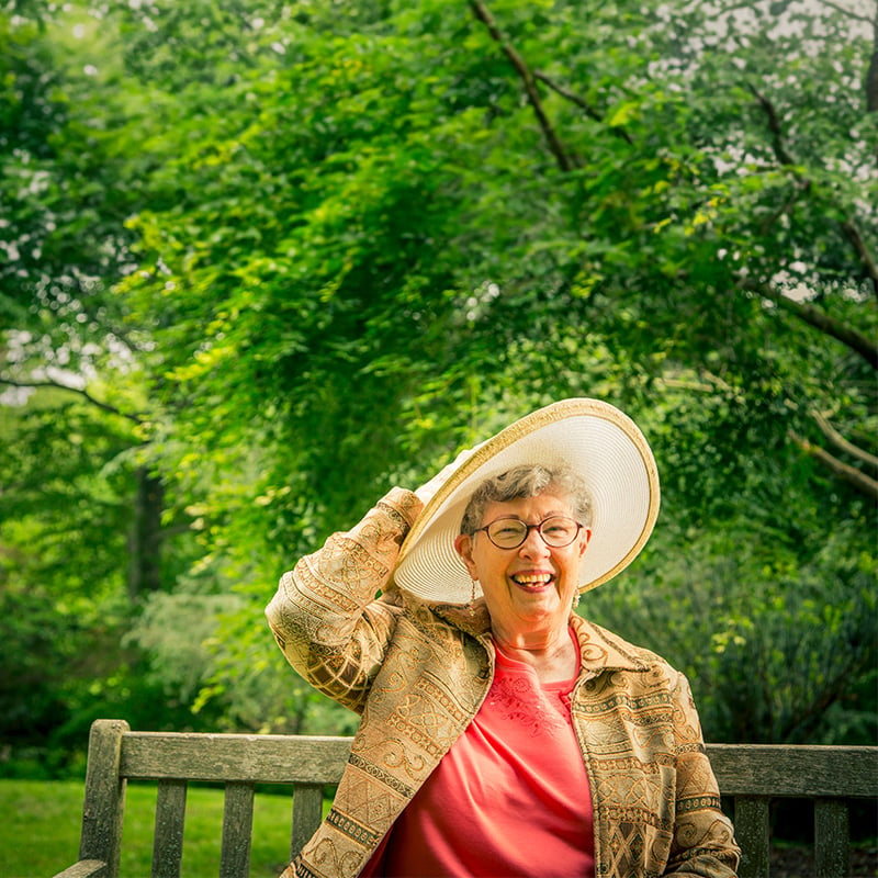 Senior woman wearing sun hat while smiling and sitting on an outdoor bench