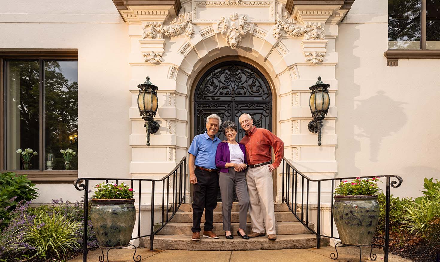 Three seniors posing on the steps outside mansion doors