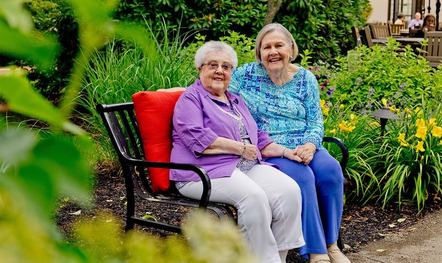 Two senior women sitting on a bench outside in a beautiful courtyard