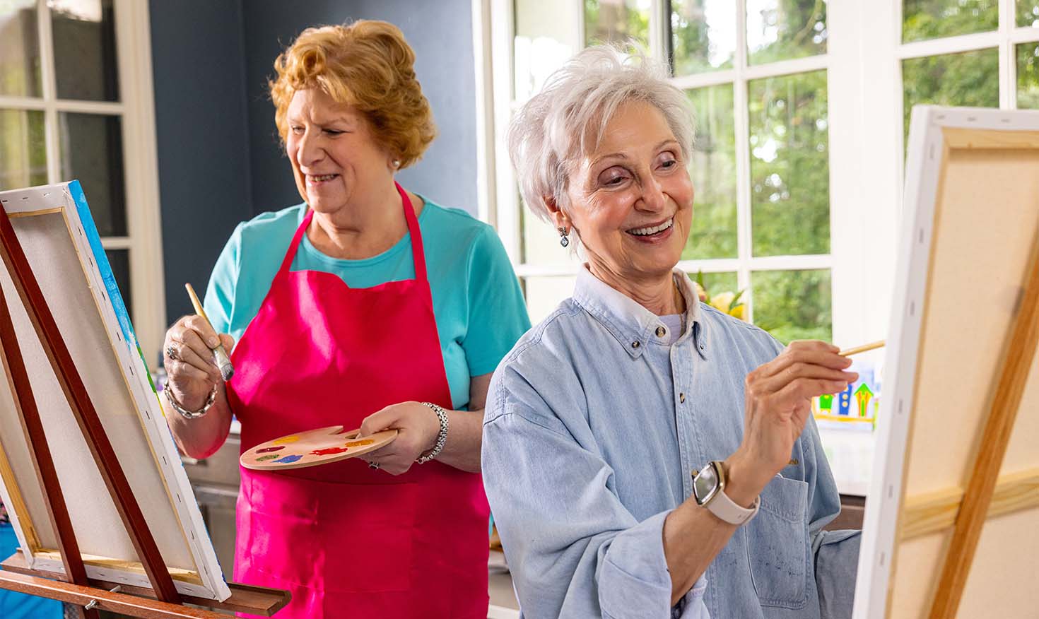 Two senior women painting on easels in art studio