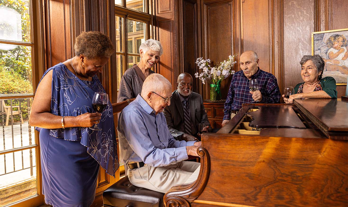 Senior friends gathered around a senior man playing music on a piano