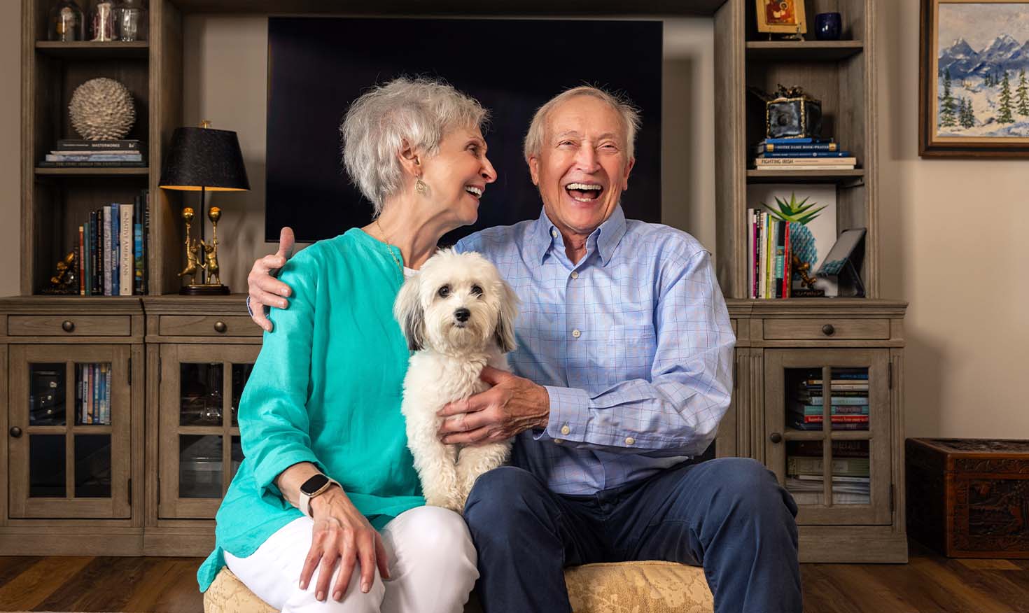 Senior couple smiling in living room with their small dog