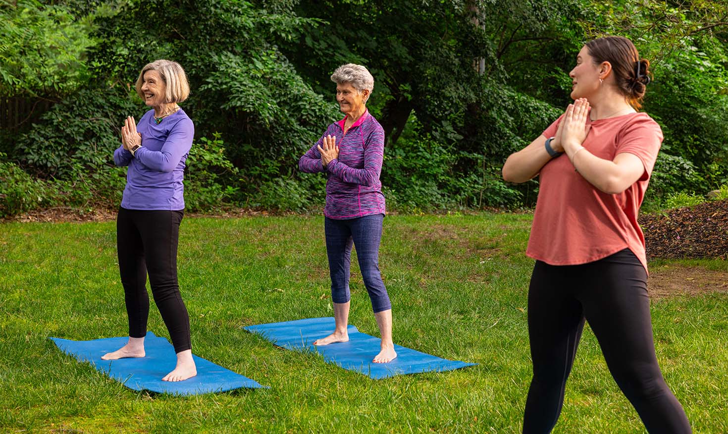 Two senior woman doing yoga outside with an instructor