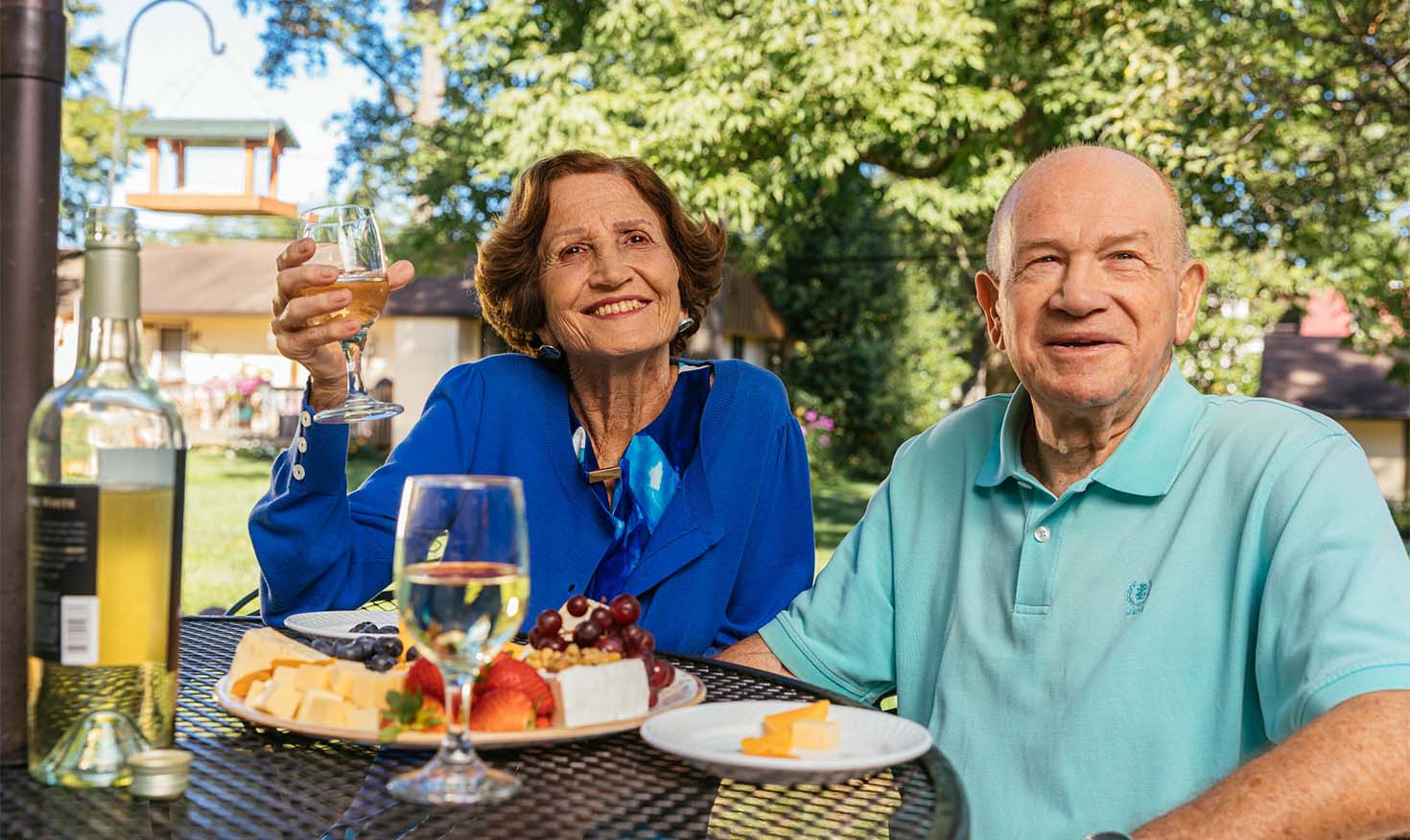 A senior woman and man enjoying wine and cheese board outside