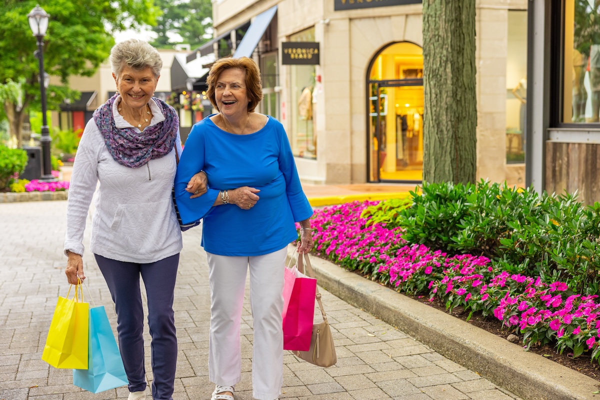 Two senior women with linked arms holding shopping bags in outdoor shopping area