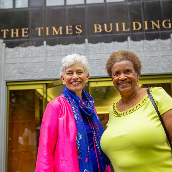 Two senior women posing outside of The Times Building on the Main Line
