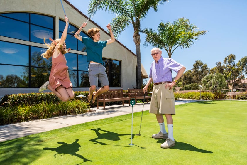 Grandfather practicing putting on green with young grandkids