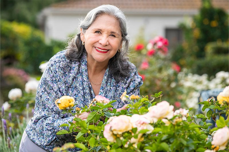 Senior woman outside smiling next to flowers