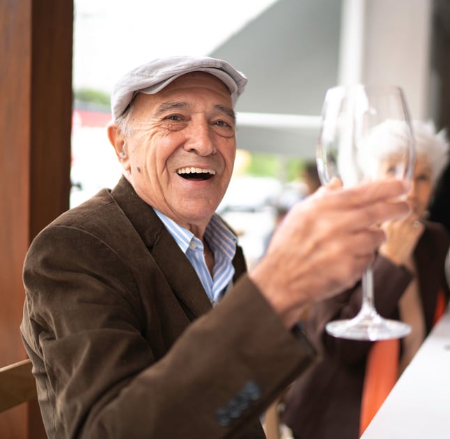 senior man sitting in a restaurant holding up wine glass