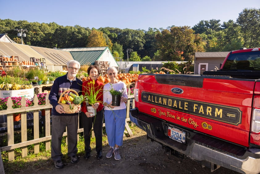 Senior man holding basket of produce and two senior women holding plants next to a red truck at Allandale Farm