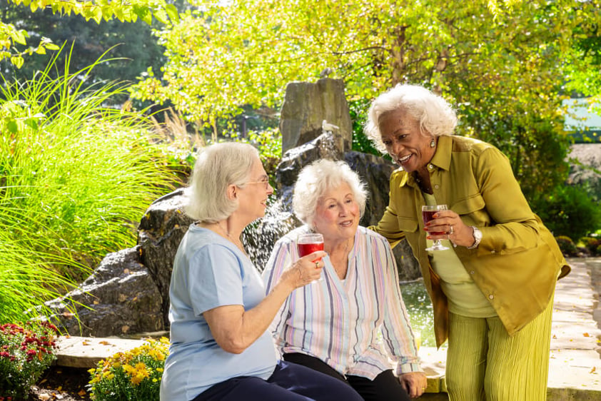 Three senior women holding wine glasses and talking on patio