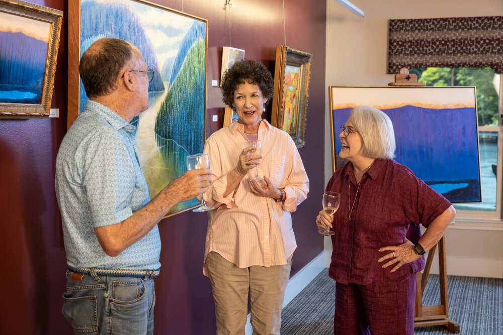 Two senior women and a senior man drinking wine in an art gallery