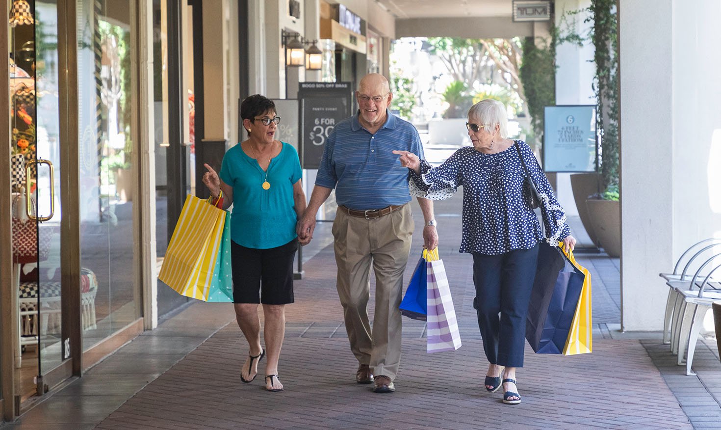 Two senior women and a senior man walking through a shopping area holding shopping bags