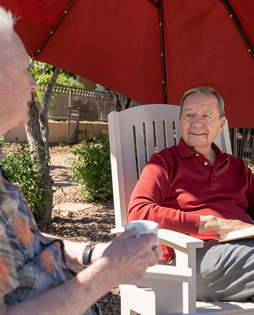 Senior man sitting under a red outdoor umbrella with a book in his lap