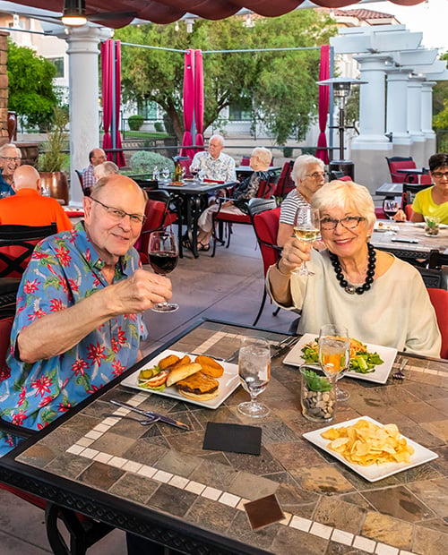 Senior couple having lunch on outdoor patio toasting the camera with wine