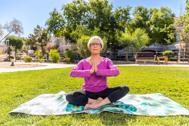 Senior woman in a bright pink shirt doing yoga outside
