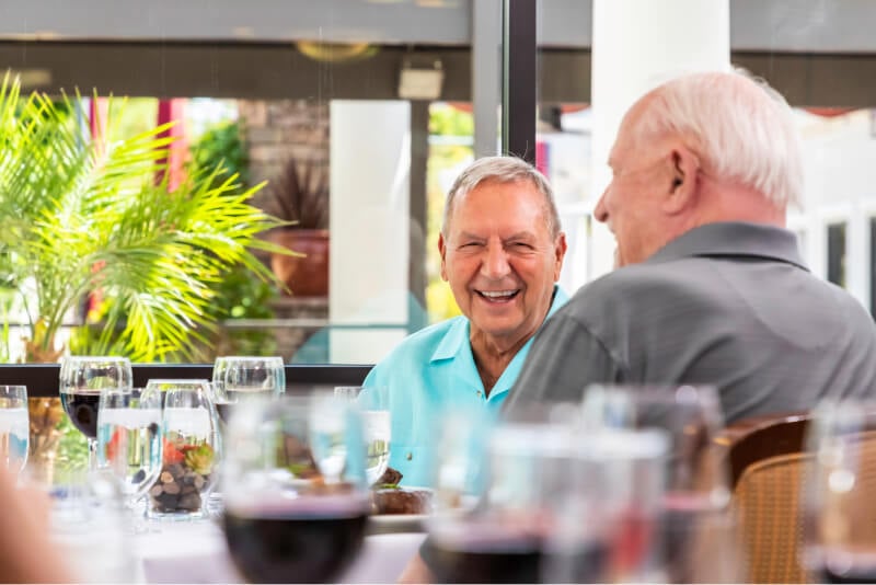 Two laughing senior men at an outdoor dining table