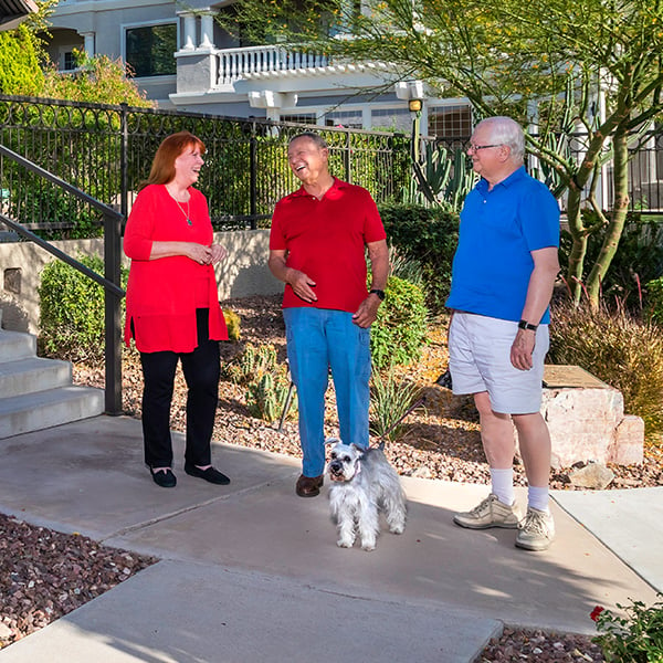 Two senior men and a senior woman with a small dog chatting outside on the sidewalk