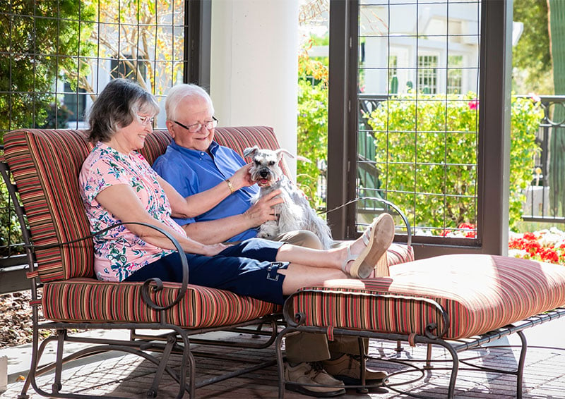 Senior couple sitting on outdoor furniture while petting a small dog
