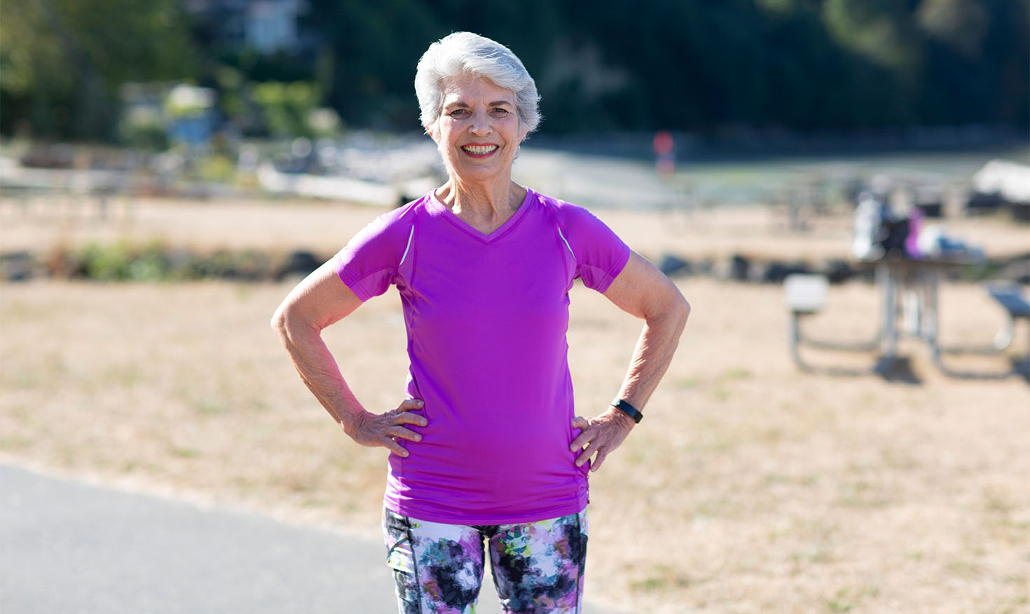 Smiling senior woman in workout clothes standing outside with her hands on her hips