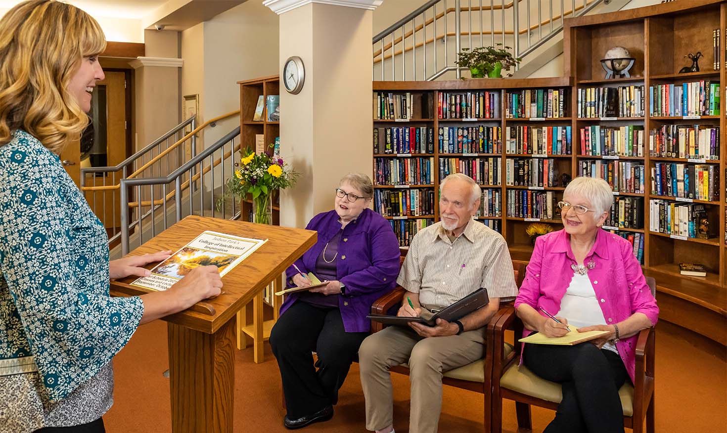 Three seniors listening to  a presentation by a woman at a lectern