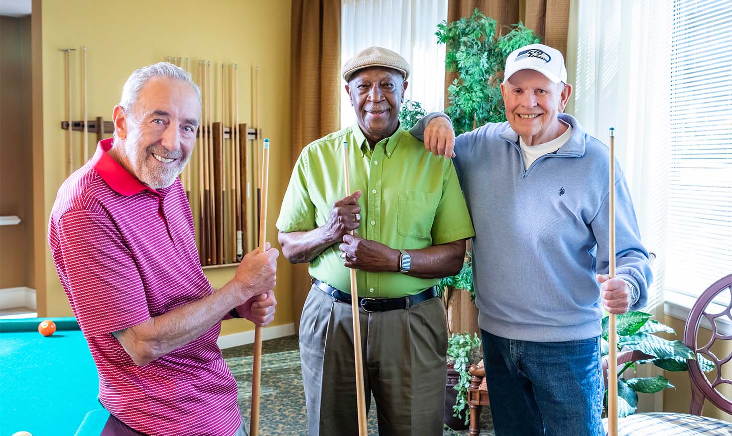 Three senior men holding pool cues standing by a pool table