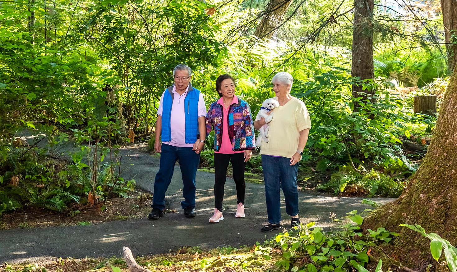 Senior couple holding hands walking on a path with a senior woman holding a small white dog