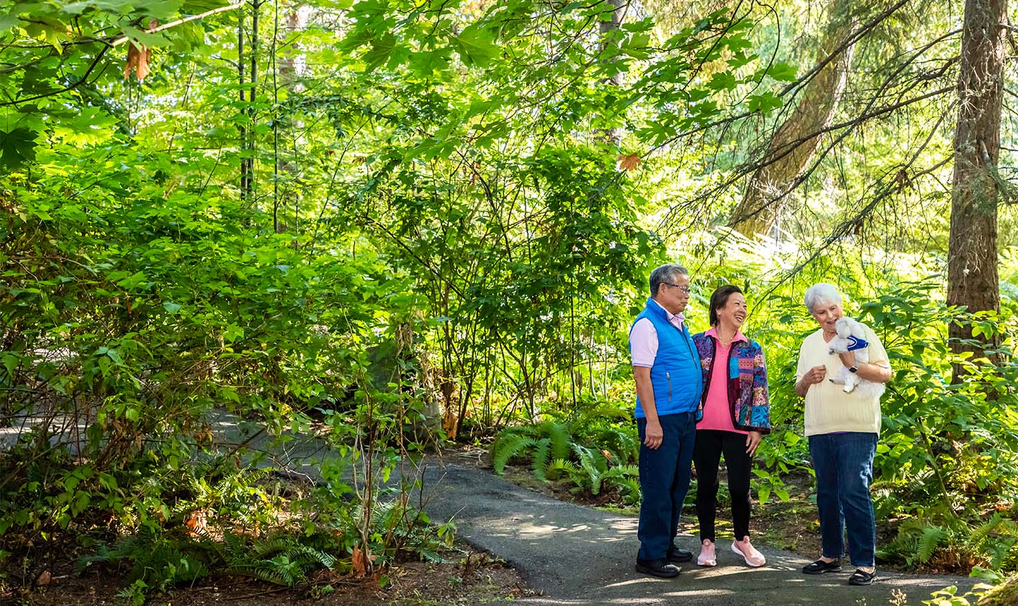 Senior couple on a path chatting with a senior woman holding a small white dog