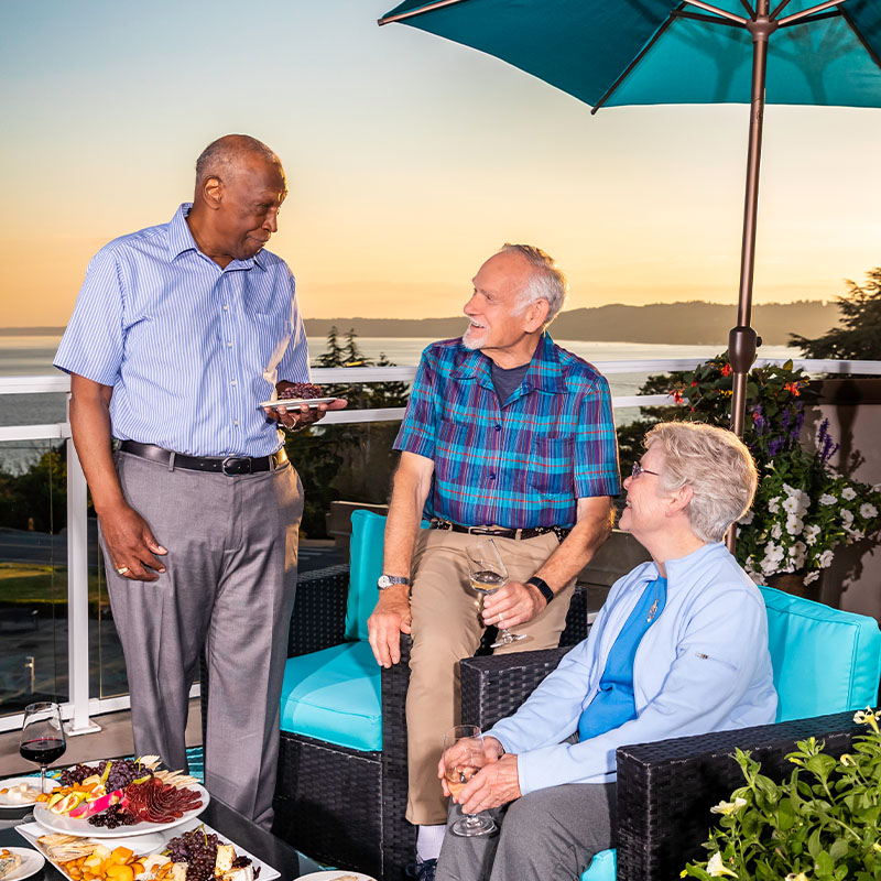 Three seniors chatting on a balcony overlooking the water at Judson Park