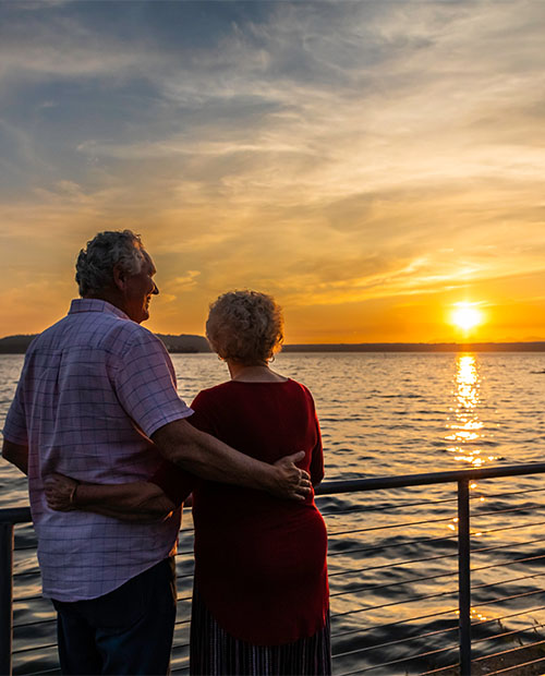 Senior couple with their arms around each other enjoying the sunset over the water