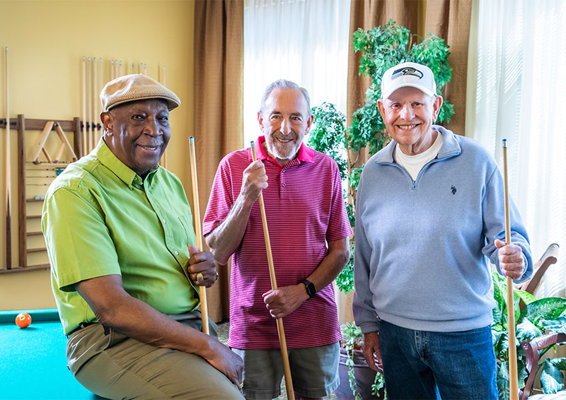 Three senior men holding pool cues standing by a pool table