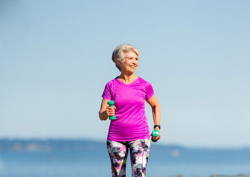 Senior woman walking while holding dumbbells 