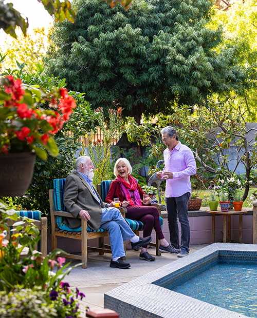 Senior man standing and talking to a senior couple sitting in an outdoor seating area at Piedmont Gardens