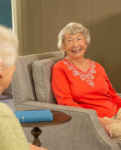 Senior woman sitting in an armchair in a common area at Piedmont Gardens