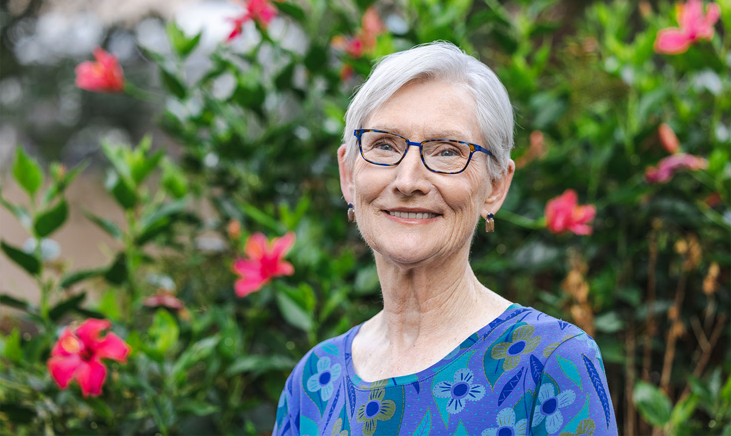 Smiling senior woman standing outside in front of flowering bush
