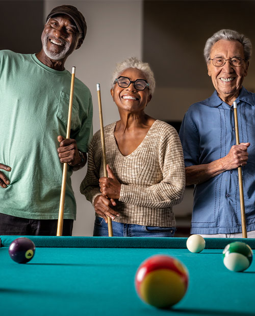 Two senior men and a senior woman holding pool cues next to a pool table