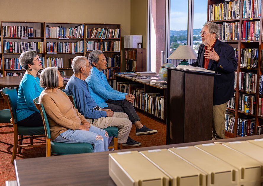 Senior man at a podium in the library lecturing to crowd of seniors