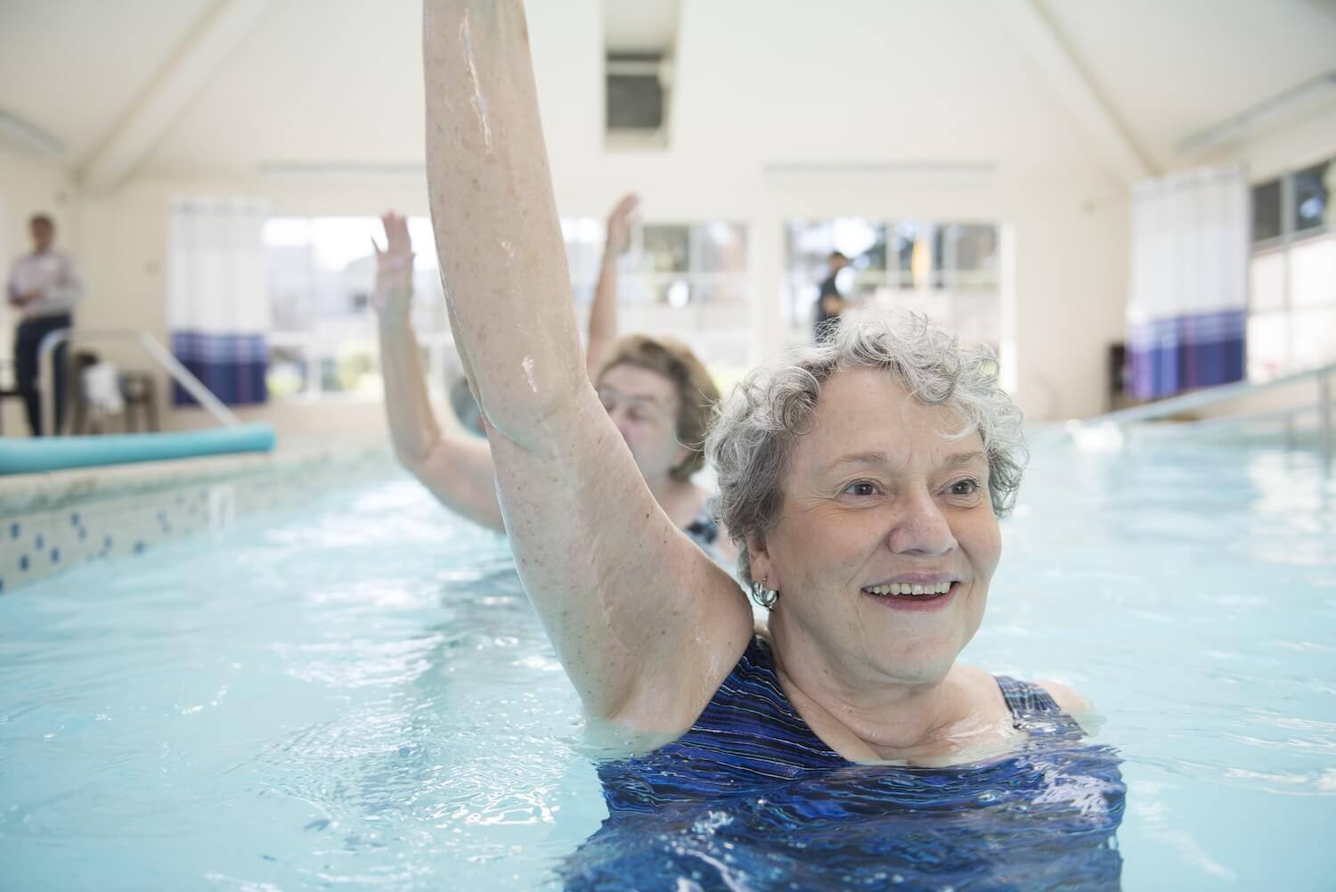 Senior woman doing water aerobics in an indoor pool at Redwood Terrace with more seniors in the background